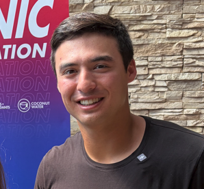 Anthony Volpe Young man smiling, wearing a dark shirt, with a stone wall background.