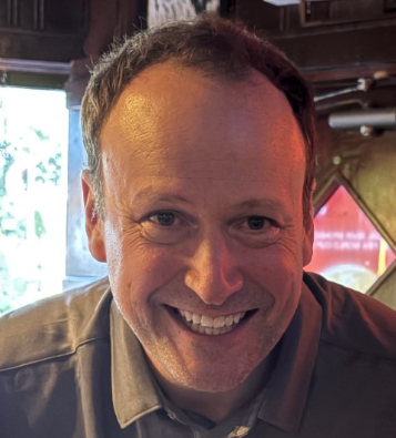 Chuck Weber Smiling man with short hair, wearing a collared shirt, in a warmly lit indoor setting.