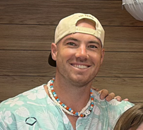 Grandy Morgan Smiling man in a floral shirt and baseball cap, wearing a beaded necklace.