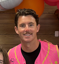 Andy Cosgrove Young man wearing a pink vest, smiling against a backdrop of colorful balloons.