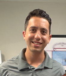 Bobby Esposito Smiling man wearing a gray shirt, standing in an office setting.